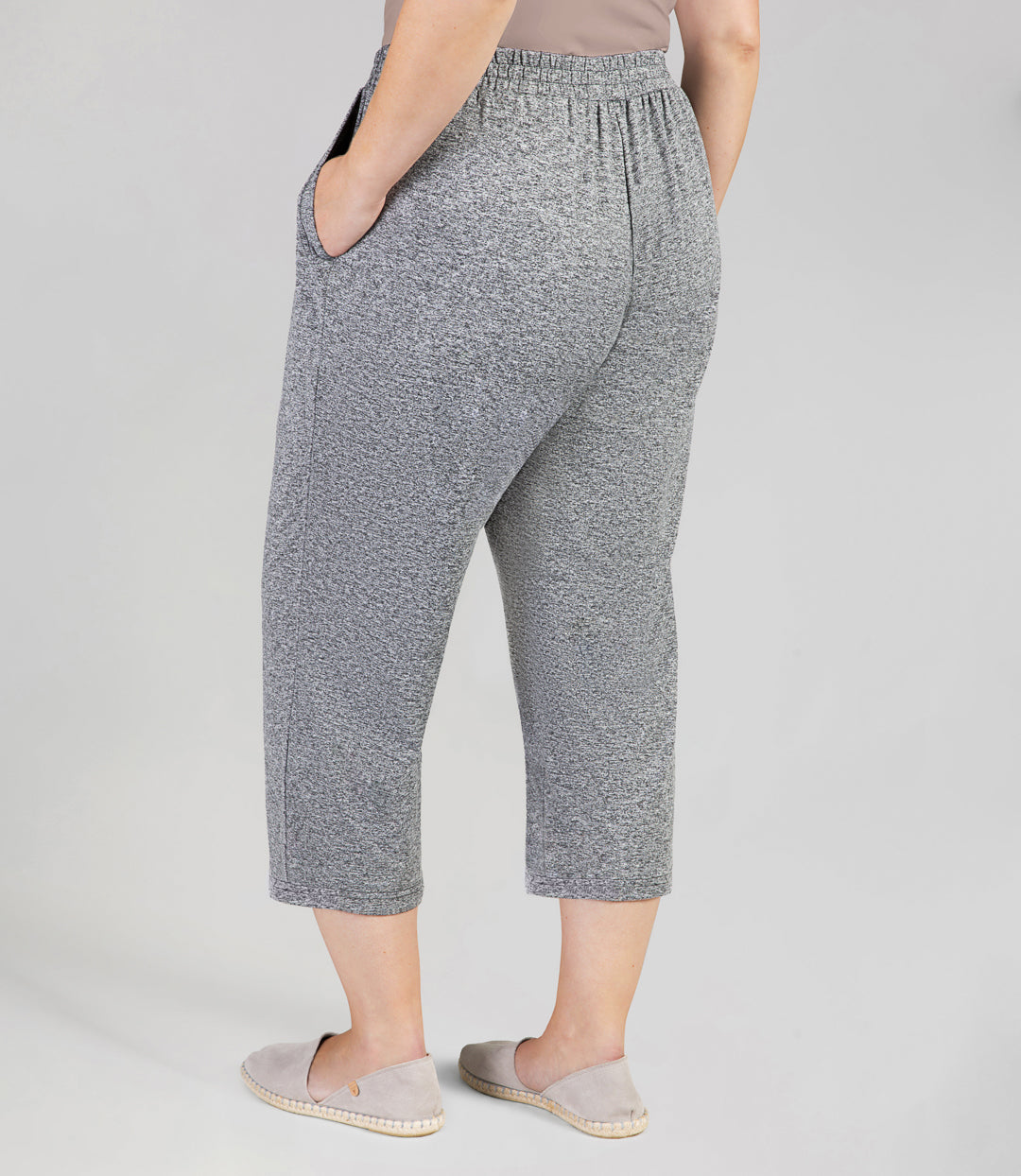 Back view, bottom half of plus sized woman, wearing JunoActives SoftWik Relaxed Fit Long Capris with Pockets in heather grey. Hemline ends at mid-calf of model.