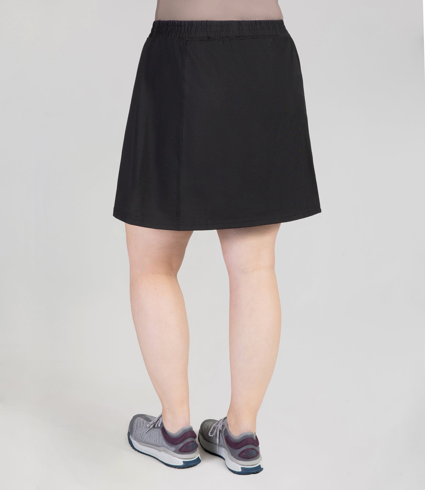 Bottom half of plus sized woman, back view, wearing JunoActives Quikwik lite skirted short in color black. Skirt hem is a few inches above knee.