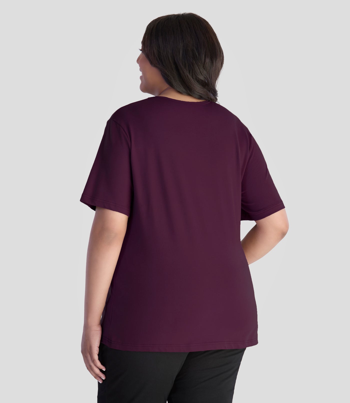 JunoActive model wearing EasyLuxe Classics V-Neck Plus Size Top in color wine. Model is facing back with her left arm by her side and right hand on hip.