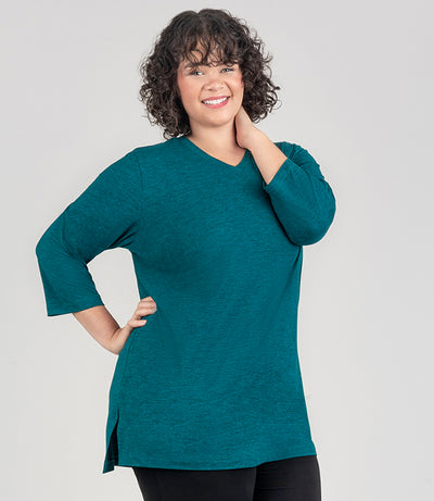 JunoActive model facing front, wearing SoftSupreme V Neck 3-4 sleeve tunic in color dark heather teal. Her right arm is bent with her hand on hip and left arm bet with hand resting on left side of neck. Tunic is longer in back with a side slit.