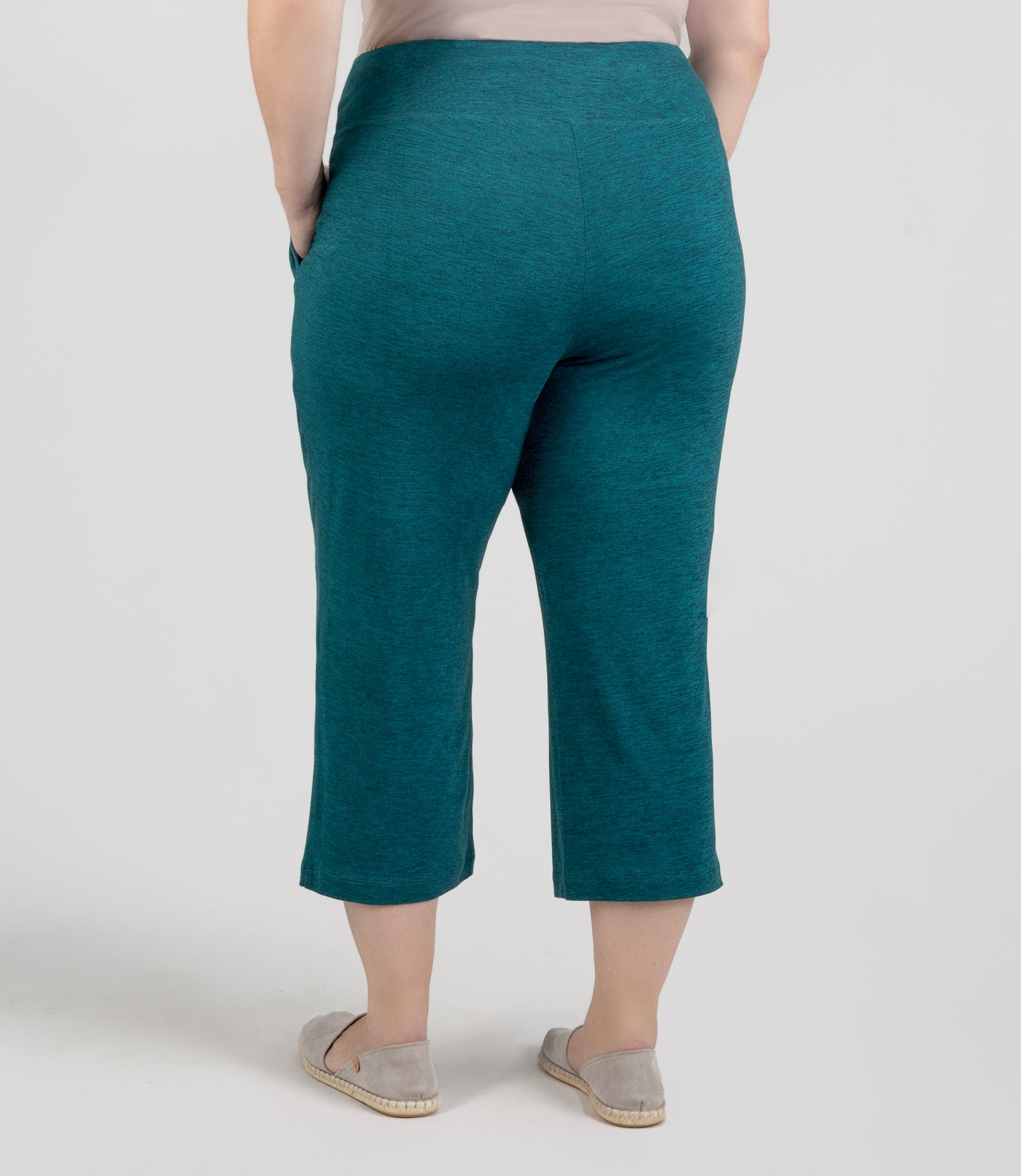 JunoActive model, facing back, wearing SoftSupreme Pocketed Lounge Capri in color heather dark teal. Left hand in pocket of capri and right arm hanging by side.