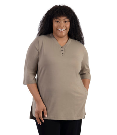 JunoActive Model wearing Stretch Naturals Lite 3/4 Sleeve Button Henley, facing front, one hand in pocket of shirt and other by her side. Color Beachwood.