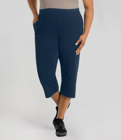 Plus size woman is facing forward, right hand in pocket, left arm and hand to side, wearing JunoActive Stretch Naturals side pocket capri. The hemline comes to mid-calf and hugs the body without being skin tight. Color is indigo.