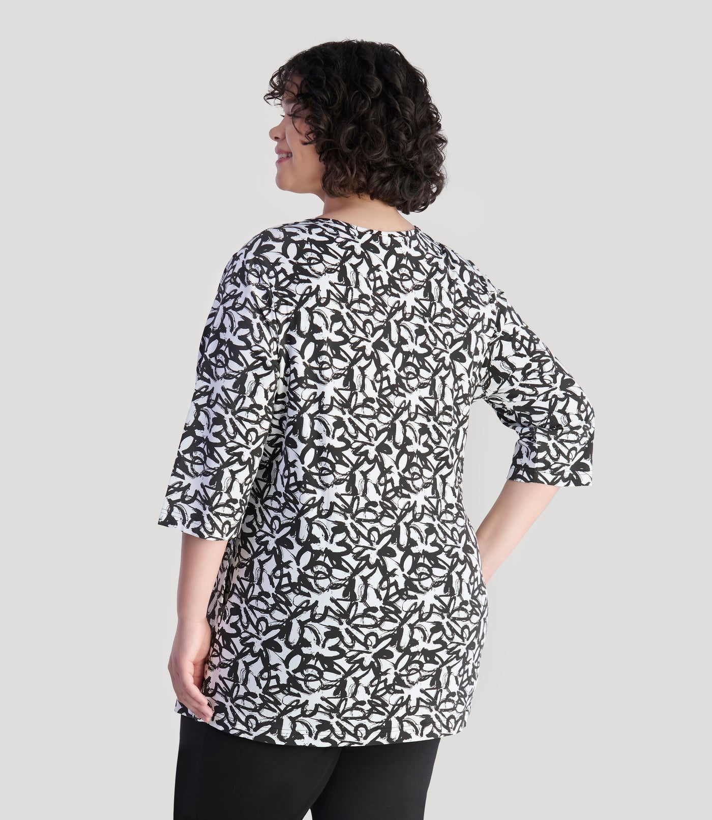 Model, facing back, wearing JunoActive's Junonia Lifestyle Cotton Printed 3/4 sleeve pocket tunic in pattern black and white wildflower.