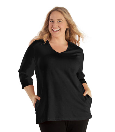 Plus size woman, facing front, wearing JunoActive plus size SoftWik V-Neck ¾ Sleeve Top with Pockets in the color Black. She is wearing JunoActive Plus Size Leggings in the color Black.