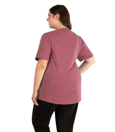 Plus size woman, facing back looking to the left, wearing JunoActive plus size QuikLite Scoop Neck Short Sleeve top in the color Roseate. She is wearing JunoActive Plus Size Leggings in the color black. 