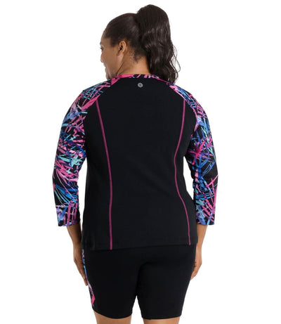 Plus size woman, back view, wearing AquaSport Long Sleeve Rash Guard Sunset Palms Print Black. Pink, blue and teal abstract line print colorblock accent on shoulders. 7/8 length sleeves and pink princess seams. JunoActive logo at top of back.