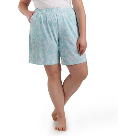 Bottom half of plus sized woman, facing front, wearing JunoActive JunoBliss Pocketed Sleep Shorts Spring Blue Floral Print. These shorts are longer and hemline comes to a few inches above knees and have pockets on both sides.