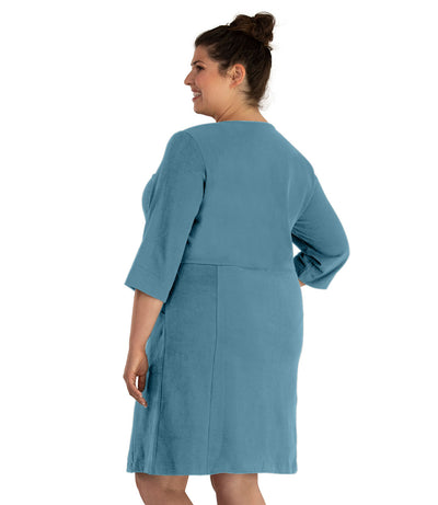 Plus size woman, facing back looking left, wearing JunoActive plus size Legacy Cotton Casual ¾ Sleeve Dress in the color Arctic Blue. Her right hand is in the dress pocket at her hip and her left hand falls naturally at her side. The dress length is at her knee.