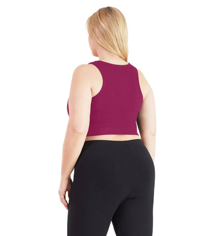 Plus size woman, facing back, wearing JunoActive plus size Stretch Naturals V-Neck Bra top in Merlot. The woman is wearing black JunoActive plus size leggings. Her arms fall naturally to her side.