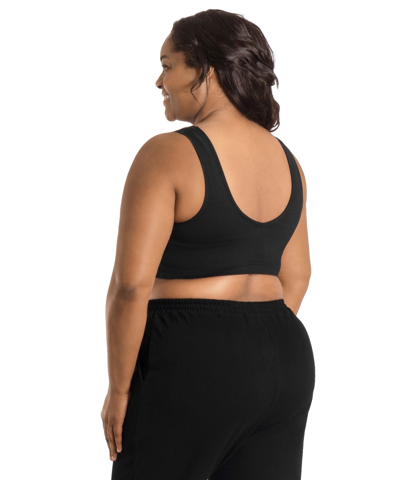 Plus size woman, facing back, wearing JunoActive Stretch Naturals Shirred Bra Top. Bra is gathered in middle on front and is a scoop top neck and scoops in back showing upper back. Straps are wide and bra color is black.