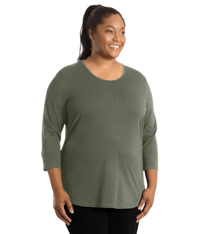 Plus size woman, facing front, wearing JunoActive’s Stretch Naturals Center Seam Scoop Neck 3/4 sleeve top in color moss green. Hands are by side. Pants are in color black. 