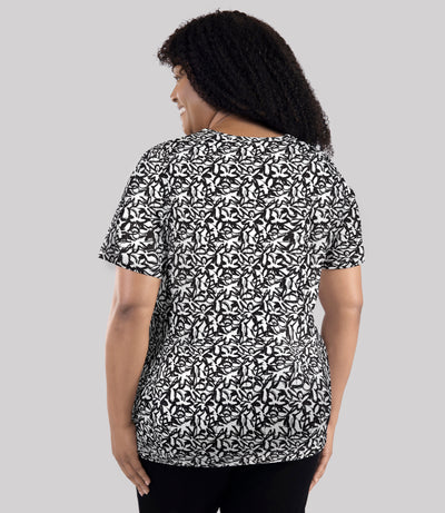 Model, facing back, wearing JunoActive's Junonia Lifestyle printed short sleeve neck top in color black and white wildflower print. 