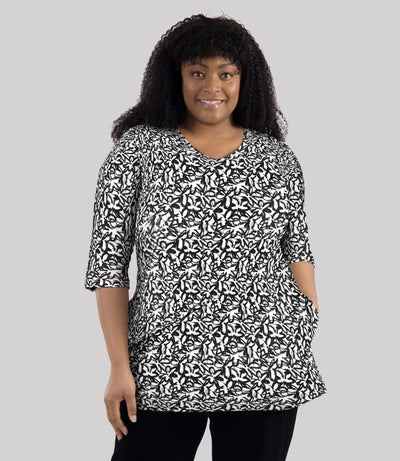 Model wearing JunoActive's Junonia Lifestyle Cotton Printed 3/4 sleeve pocket tunic in pattern black and white wildflower. Her left hand is in left pocket of shirt.