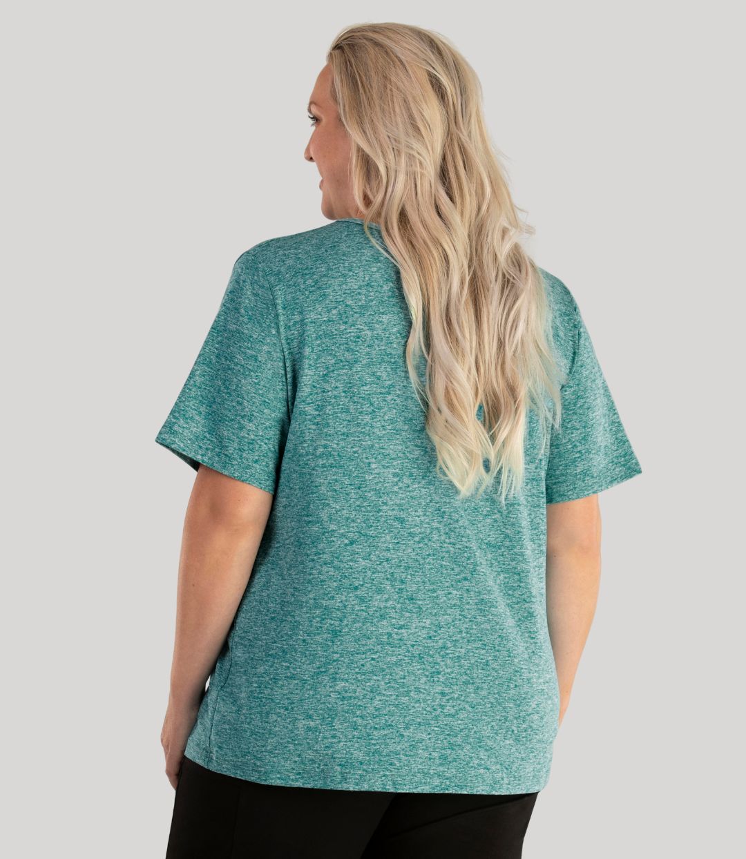 Plus size woman, facing back, wearing JunoActive plus size SoftWik V-Neck Tee in the color Heather Emerald. She is wearing JunoActive Plus Size Leggings in the color Black.