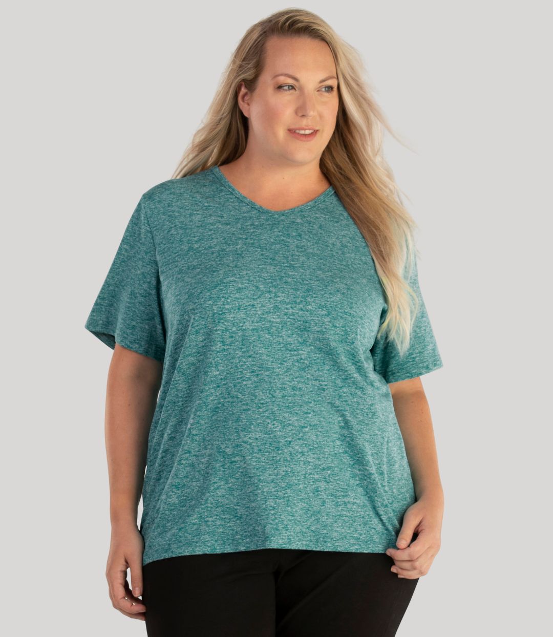 Plus size woman, facing front, wearing JunoActive plus size SoftWik V-Neck Tee in the color Heather Emerald. She is wearing JunoActive Plus Size Leggings in the color Black.