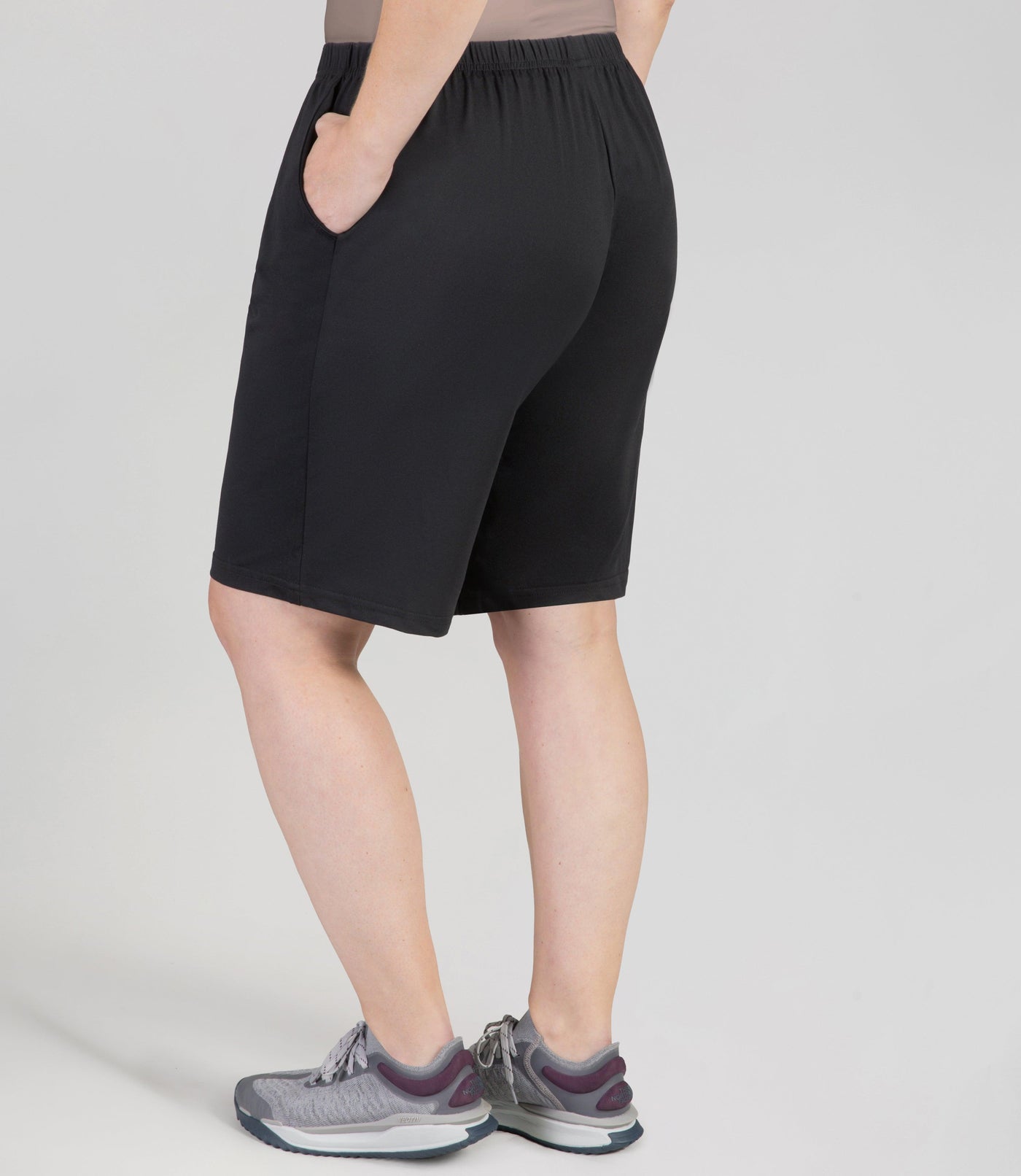 Bottom half of plus sized woman, back view, wearing JunoActive Softwik Relaxed Fit Shorts with pockets in color black. Bottom hem is about an inch above the knee.