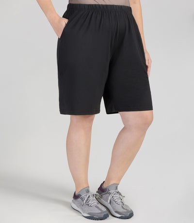 Bottom half of plus sized woman, side view, wearing JunoActive Softwik Relaxed Fit Shorts with pockets in color black. Bottom hem is about an inch above the knee.