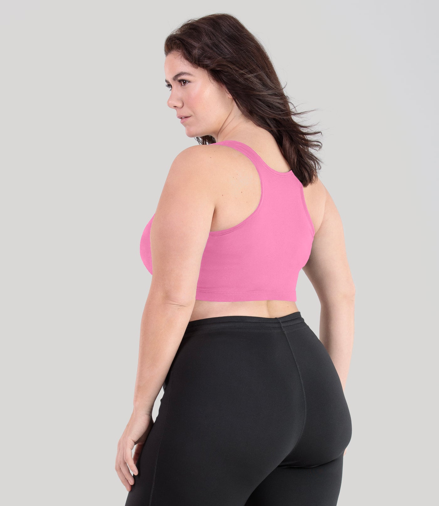 Plus size woman, facing back, wearing JunoActive plus size QuikWik Racerback Bra in Power Pink. The woman is wearing a pair of Black JunoActive leggings.