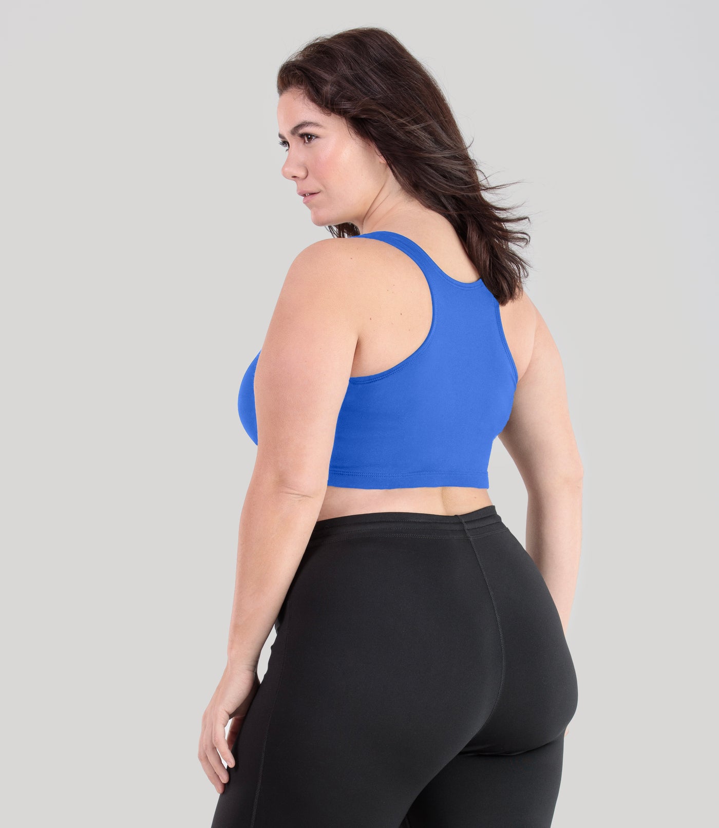 Plus size woman, facing back, wearing JunoActive plus size QuikWik Racerback Bra in True Blue. The woman is wearing a pair of Black JunoActive leggings.