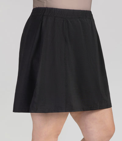 Bottom half of plus sized woman, close up side view, wearing JunoActives Quikwik lite skirted short in color black. Skirt hem is a few inches above knee.