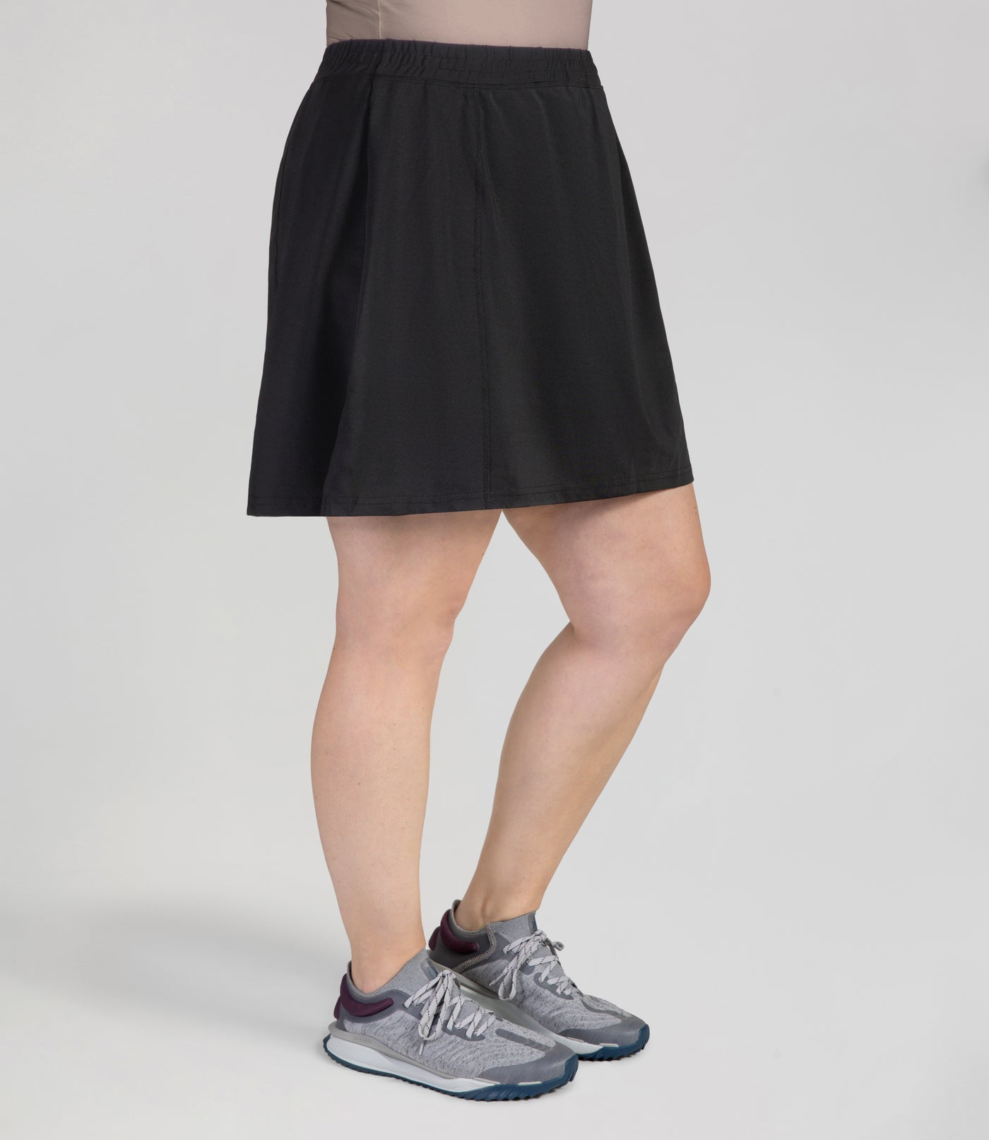 Bottom half of plus sized woman, front view, wearing JunoActives Quikwik lite skirted short in color black. Skirt hem is a few inches above knee.