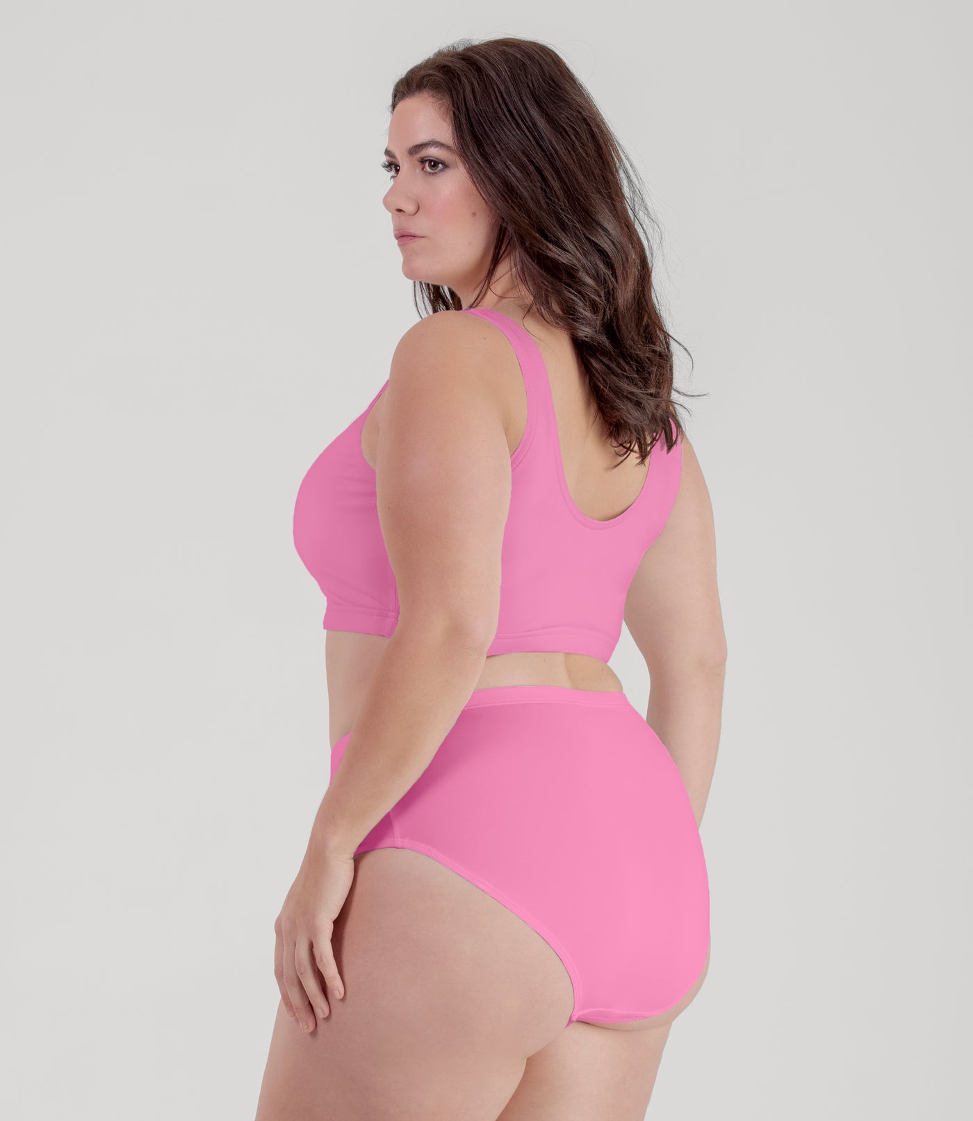 Plus size woman, facing back, wearing JunoActive plus size QuikWik Soft Control Bra Top in Power Pink.