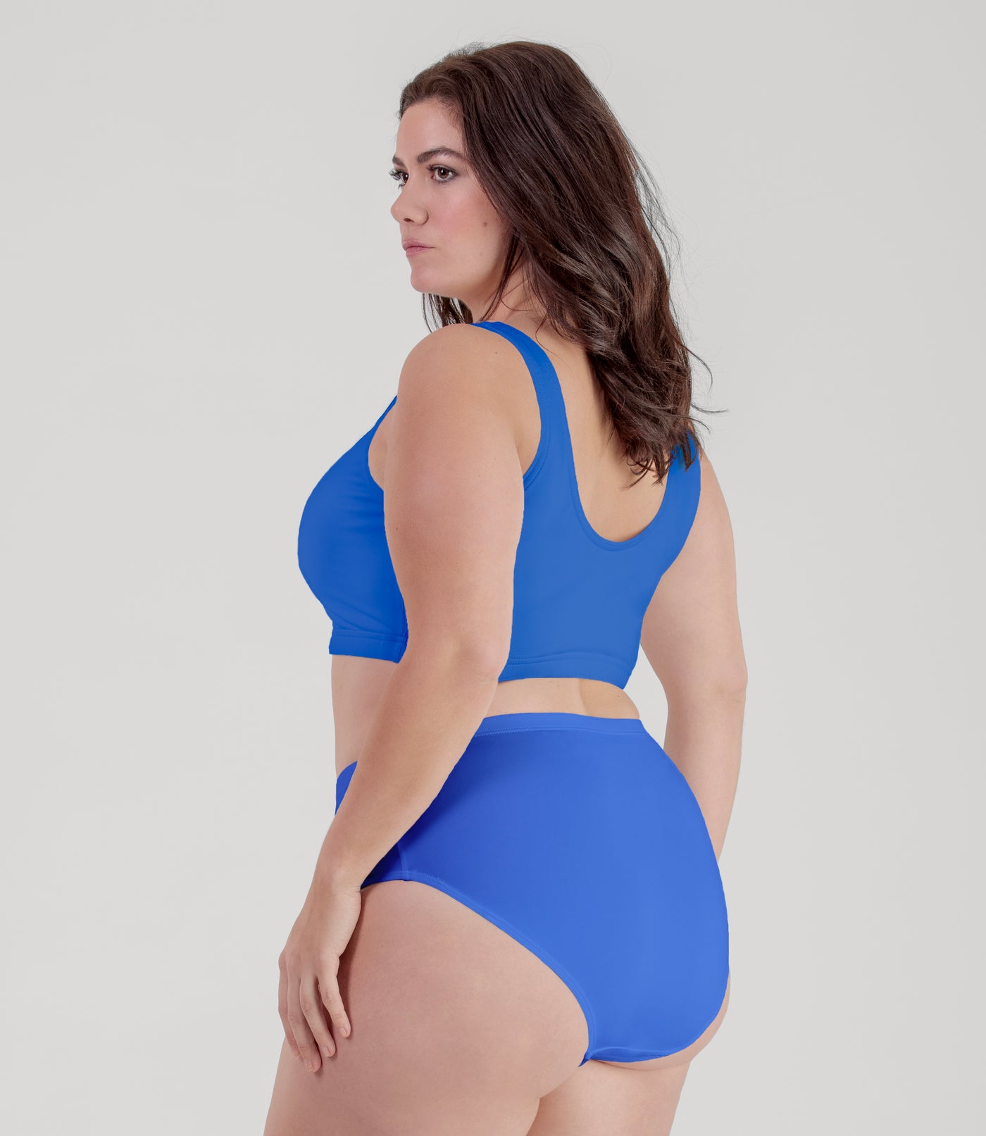 Plus size woman, facing Back, wearing JunoActive plus size QuikWik Soft Control Bra Top in True Blue.