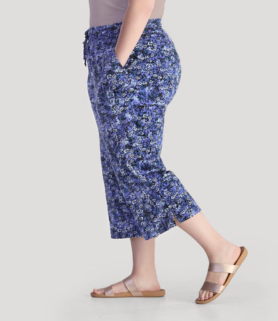 Plus size model, facing side, wearing JunoActive's EZ style cotton pocketed plus size capris in blue meadow print. 