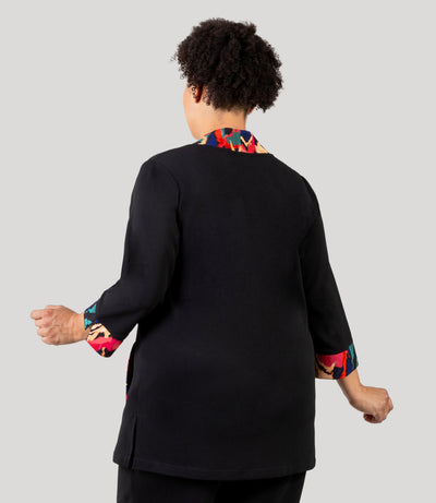 Plus size woman, facing back, wearing a JunoActive's Junonia Classic Plus size cardigan with modern ikat print on lapels and cuffs, the rest is solid black.