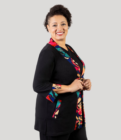 Plus size woman, facing front and side, wearing a JunoActive's Junonia Classic Plus size cardigan featuring modern ikat print on lapel and cuffs and solid black for the reminder of cardigan.