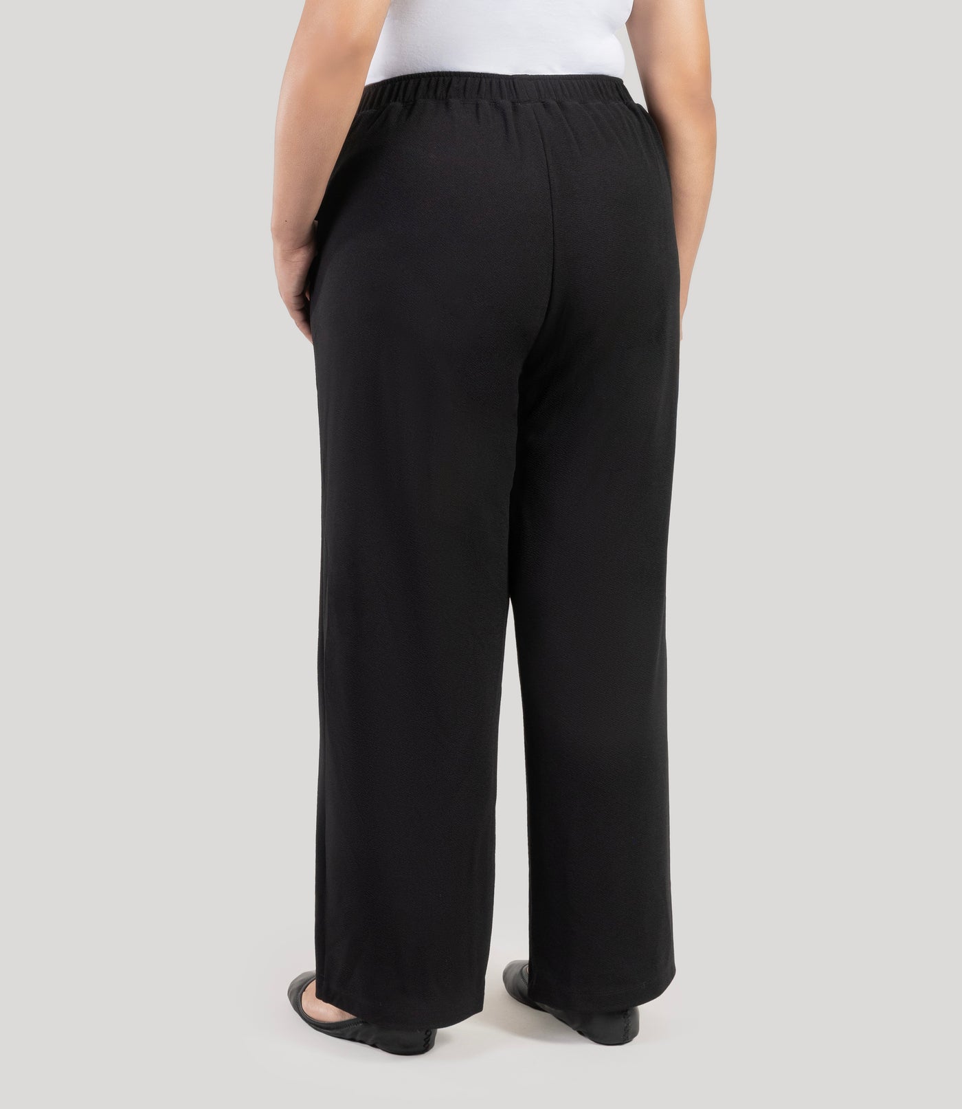 Plus size woman, facing back, wearing JunoActive's Junonia Classic Pocketed black Plus Size pants on a plain background.