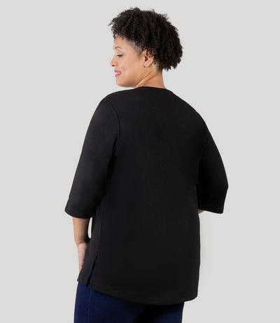 Plus Size Woman, facing back, wearing Junonia Classic 3/4 Sleeve V-Neck Tunic black Plus Size top. Top features v-neck, 3/4 sleeves and vent notches on each sleeve and side hem. 