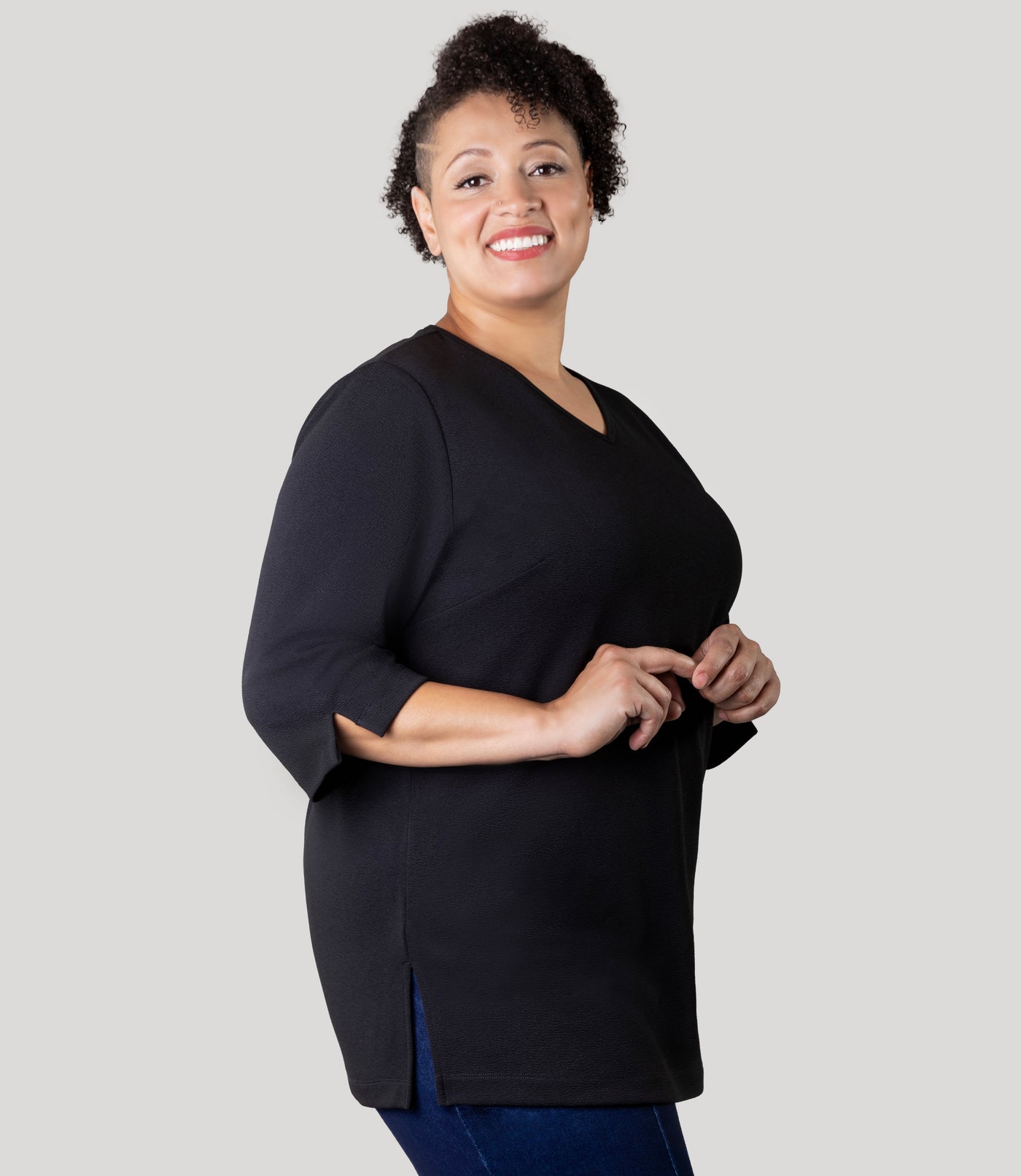 Plus Size Woman, facing side, wearing Junonia Classic 3/4 Sleeve V-Neck Tunic black Plus Size top.  Top features v-neck, 3/4 sleeves and vent notches on each sleeve and side hem.