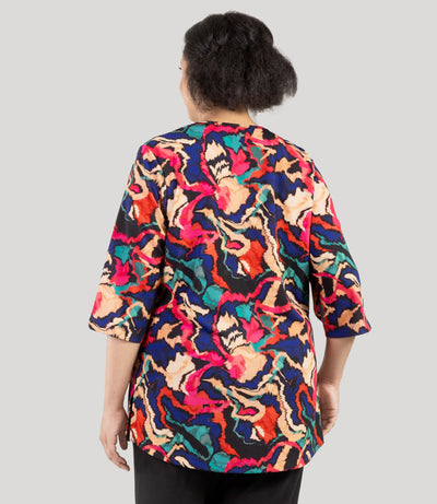 Plus size woman, facing back, wearing a JunoActive's Junonia Classic 3/4 Sleeve V-Neck Plus Size Tunic. Top features modern ikat print, v-neck, 3/4 sleeves and side vents at hem.
