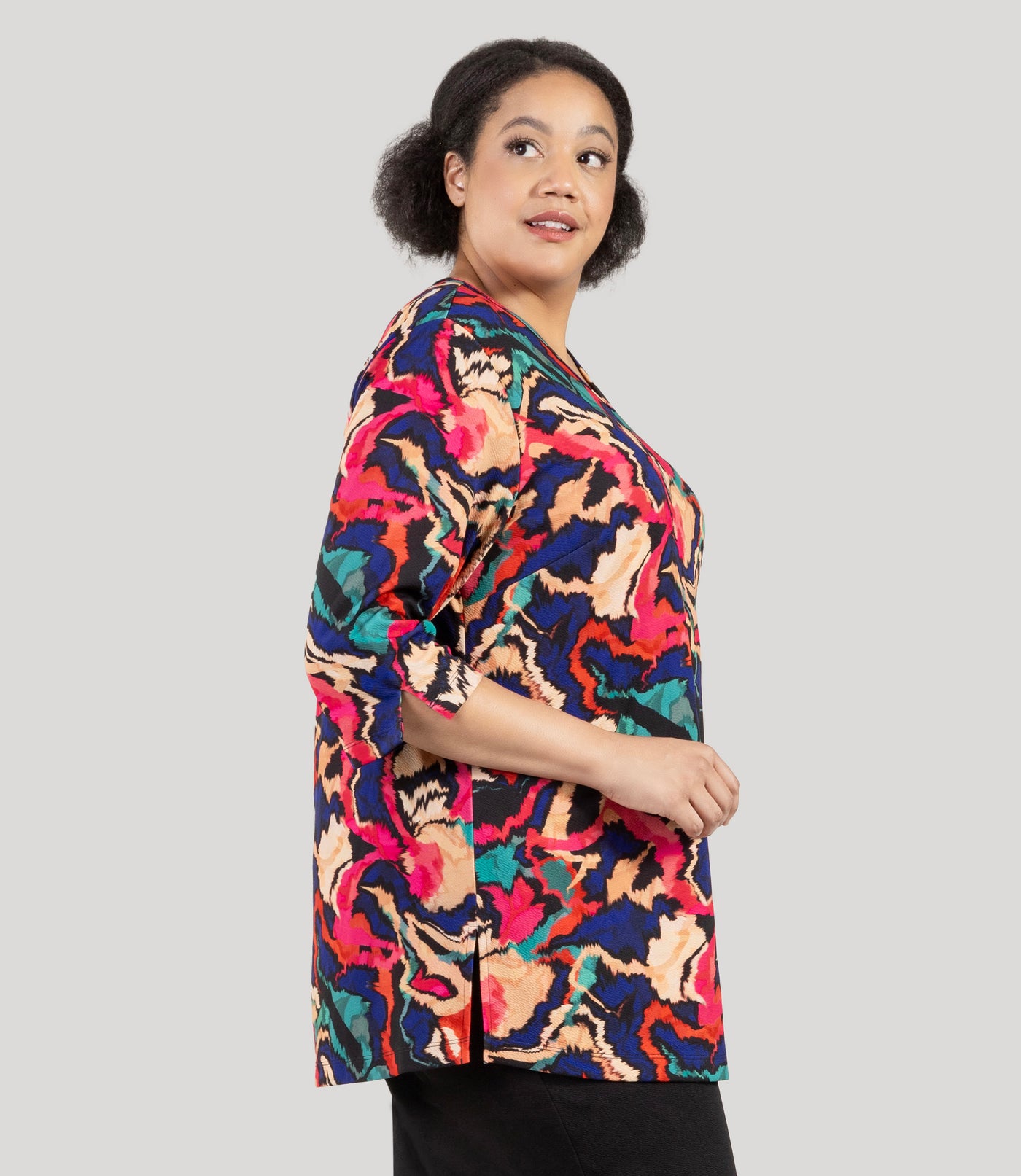 Plus size woman, facing side, wearing a JunoActive's Junonia Classic 3/4 Sleeve V-Neck Plus Size Tunic. Top features modern ikat print, v-neck, 3/4 sleeves and side vents at hem.