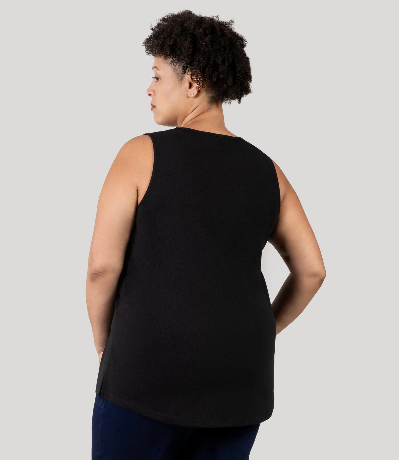 Plus size Woman, facing back wearing JunoActive's Junonia Classic Sleeveless Plus Size Top in black, featuring v-neck and side hem vents.