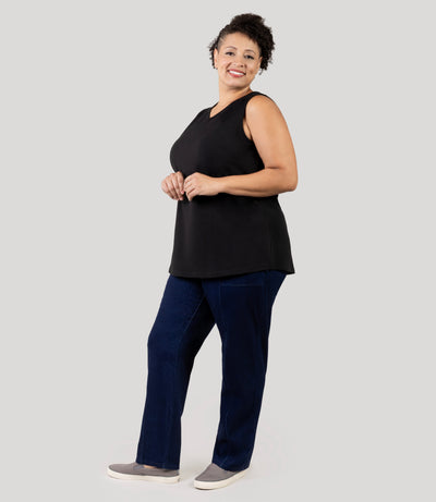 Plus size Woman, facing front and angled to side, wearing JunoActive's Junonia Classic Sleeveless Plus Size Top in black,  against a plain background. Full size image of model, head to toe. Wearing JunoActive's Stretch Twill Plus Size Bottoms. Sleeveless top features v-neck and side hem vents.