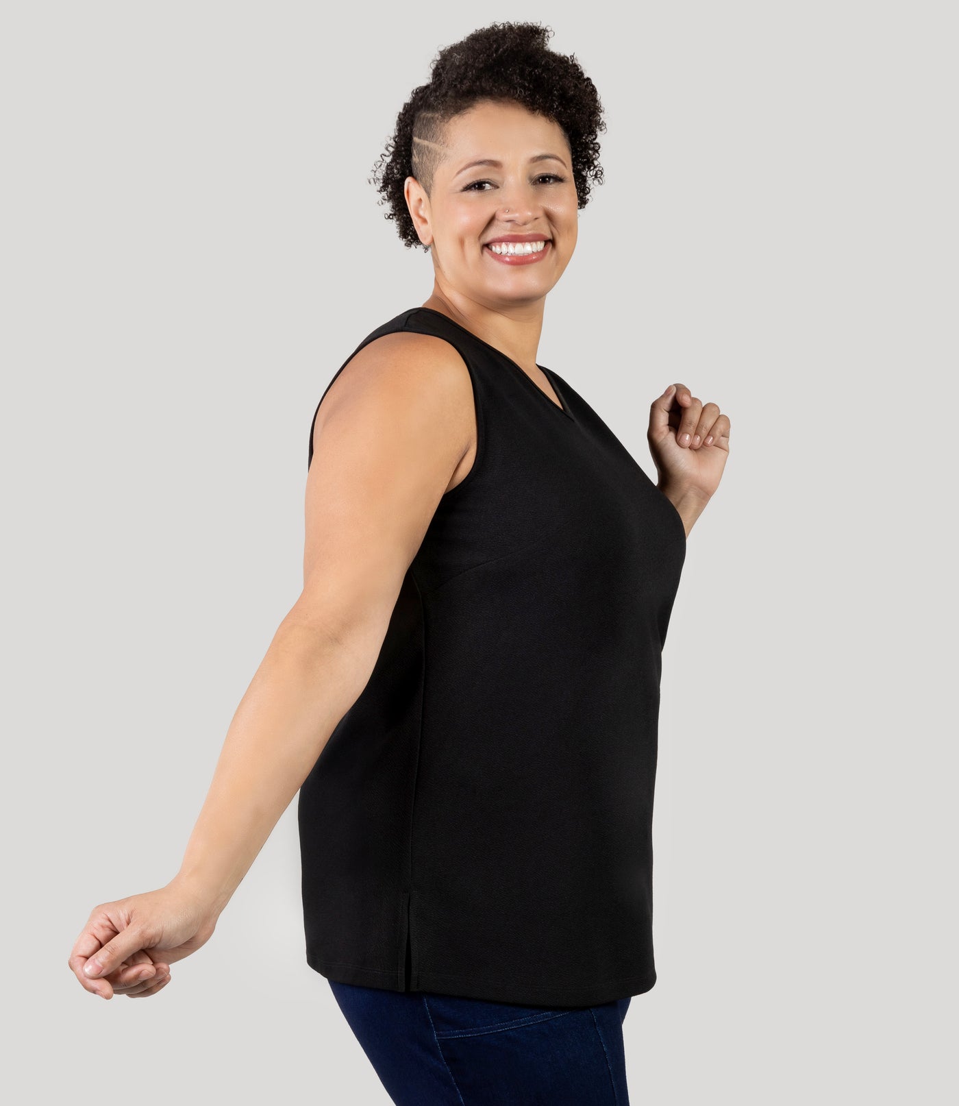 Plus size Woman, facing side, wearing JunoActive's Junonia Classic Sleeveless Plus Size Top in black, featuring v-neck and side vents.