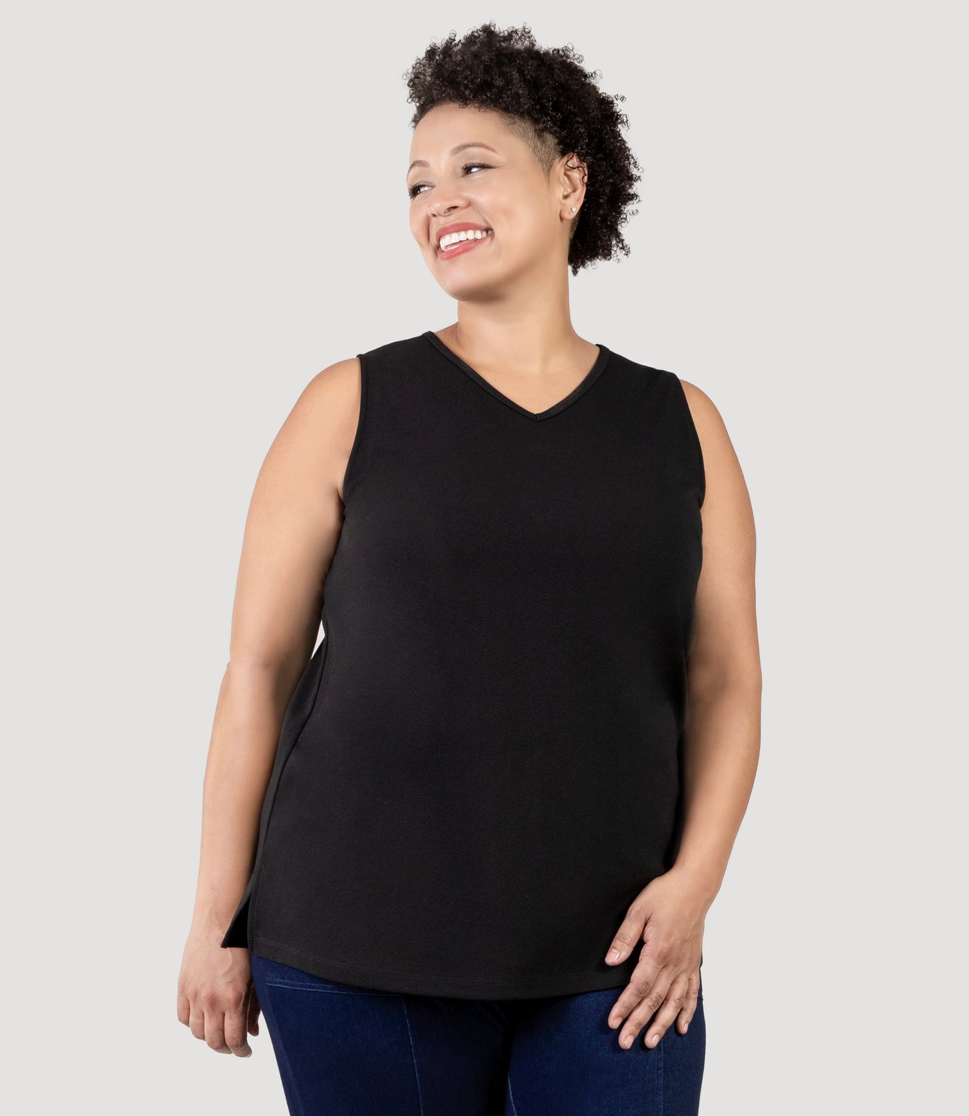 Plus size Woman, facing front, wearing JunoActive's Junonia Classic Sleeveless Plus Size Top in black. Features a v-neck and side hem vents.