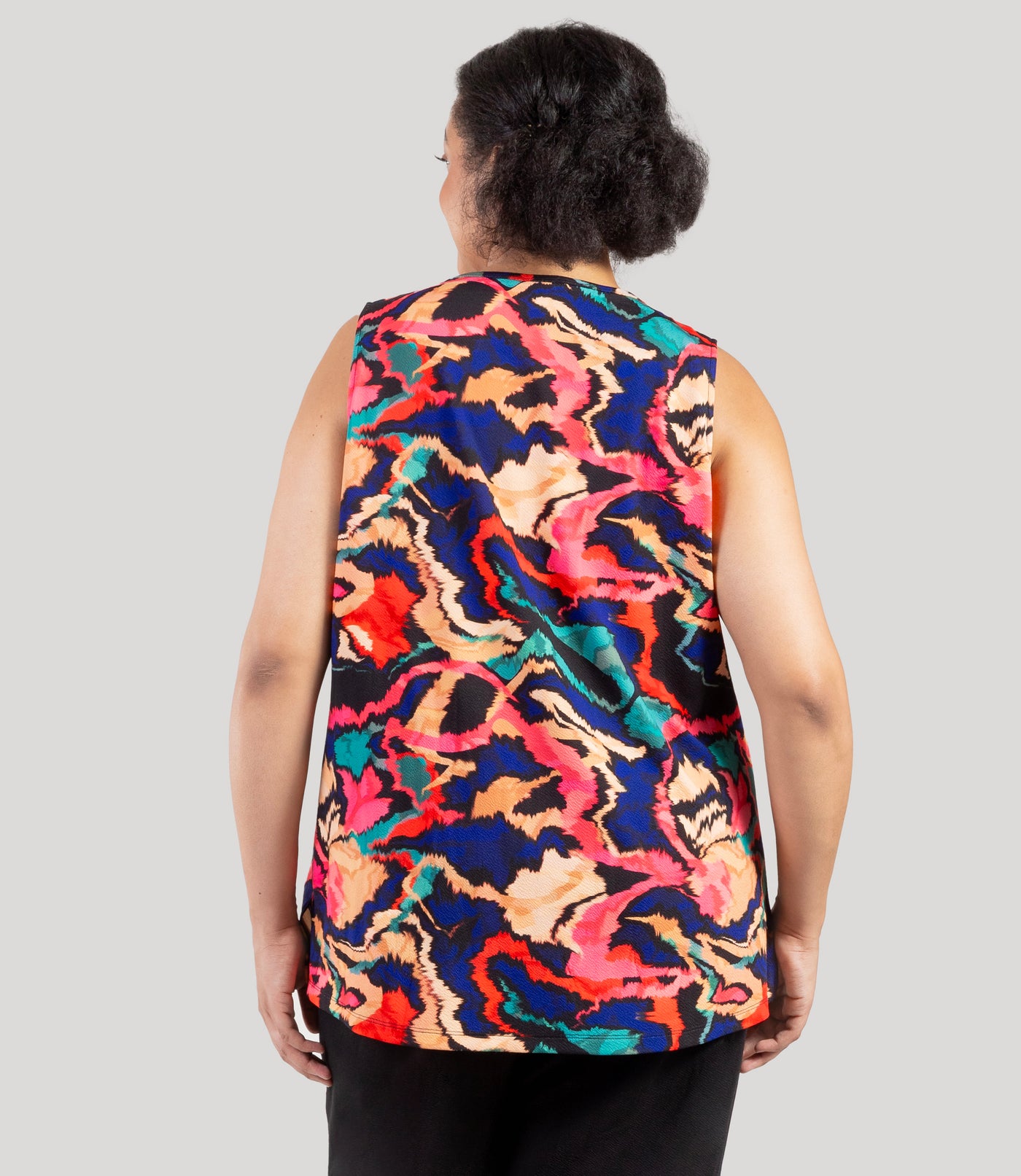 Plus size model, facing back, wearing JunoActive's Junonia Classic Sleeveless Plus Size Top in Modern Ikat print. Sleeveless top features v-neck and side vents at hem.