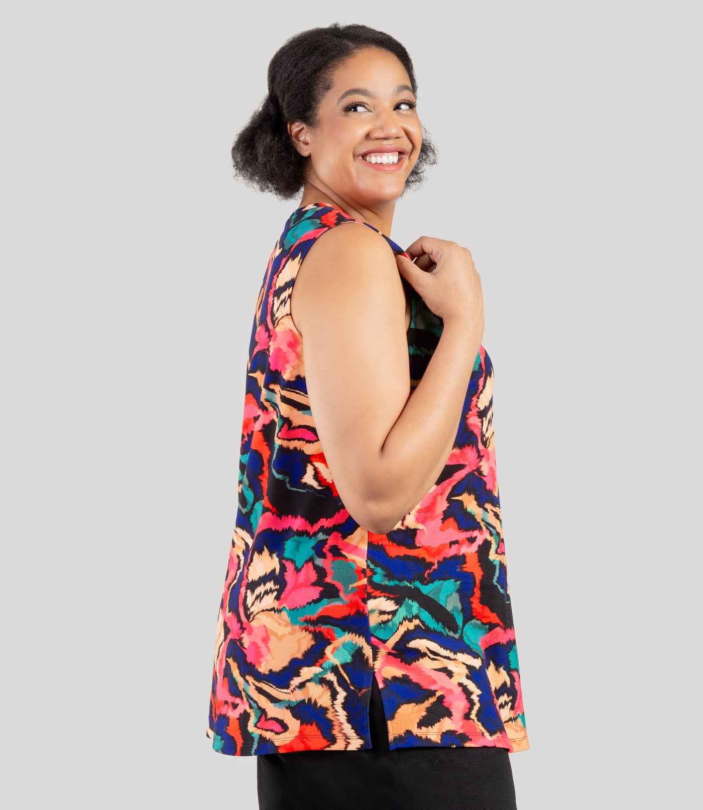 Plus size model, facing side, wearing JunoActive's Junonia Classic Sleeveless Plus Size Top in Modern Ikat print. Sleeveless top features v-neck and side vents at hem.