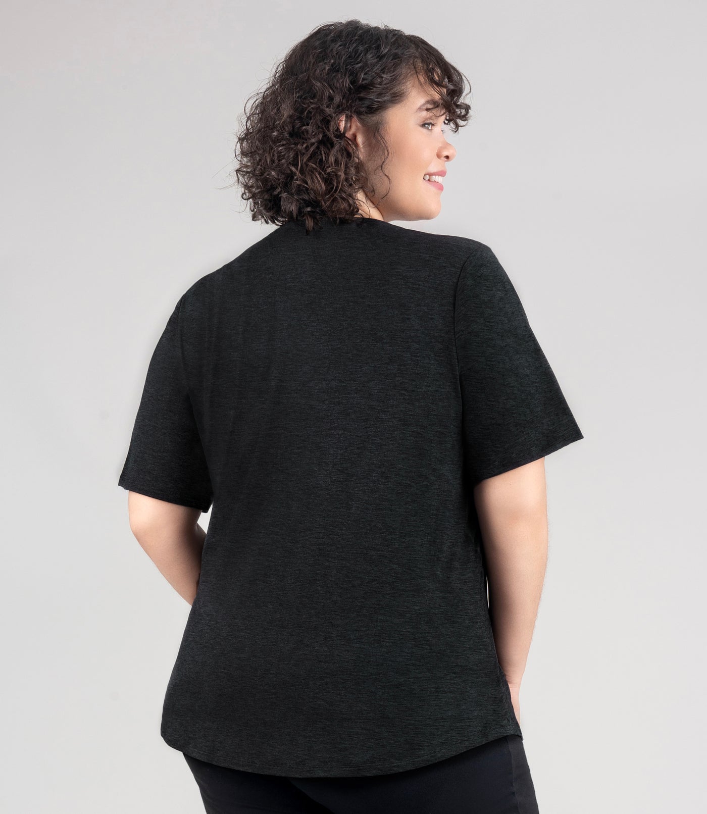 JunoActive model, facing back, wearing soft supreme scoop neck short sleeve top in color heather black. Her arms are by her side. Length of sleeve is about 1.5 inches above elbow.