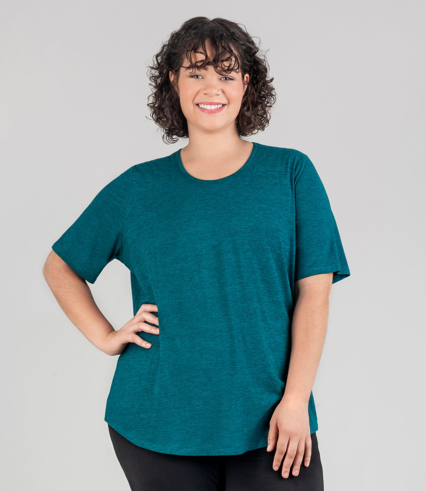 JunoActive mode, facing front, l wearing soft supreme scoop neck short sleeve top in color heather dark teal. Her right arm is bent and hand on hip and left arm is by her side.. Length of sleeve is about 1.5 inches above elbow.