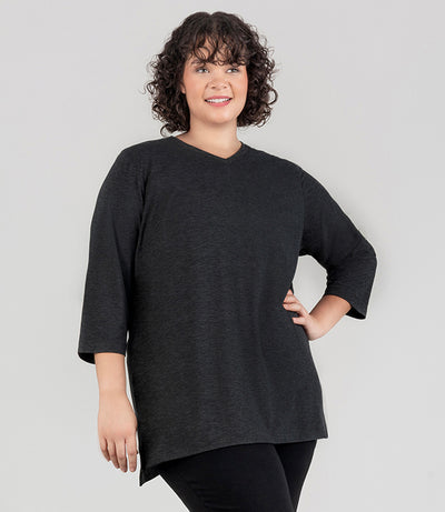 JunoActive model facing front, wearing SoftSupreme V Neck 3-4 sleeve tunic in color heather black. Her right arm is by her side and left arm is bent on her hip. Tunic is longer in back with a side slit.