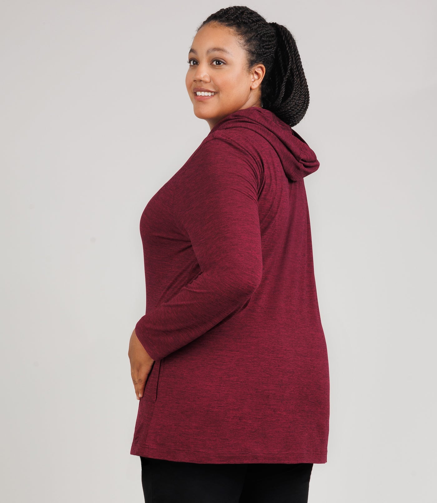 JunoActive model, facing side and back, wearing SoftSupreme Pocketed Hoodie in color Heather Cranberryl. Model's left hand is on left hip.