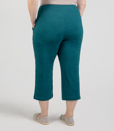 JunoActive model, facing back, wearing SoftSupreme Pocketed Lounge Capri in color heather dark teal. Left hand in pocket of capri and right arm hanging by side.
