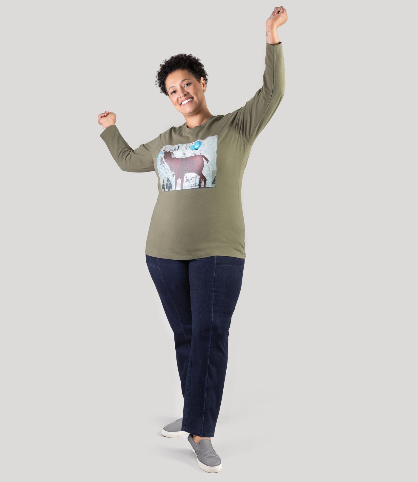 Plus size model, facing front, arms in arm, wearing Stretch Twill plus size pant in denim blue and olive long sleeve graphic plus size tee.