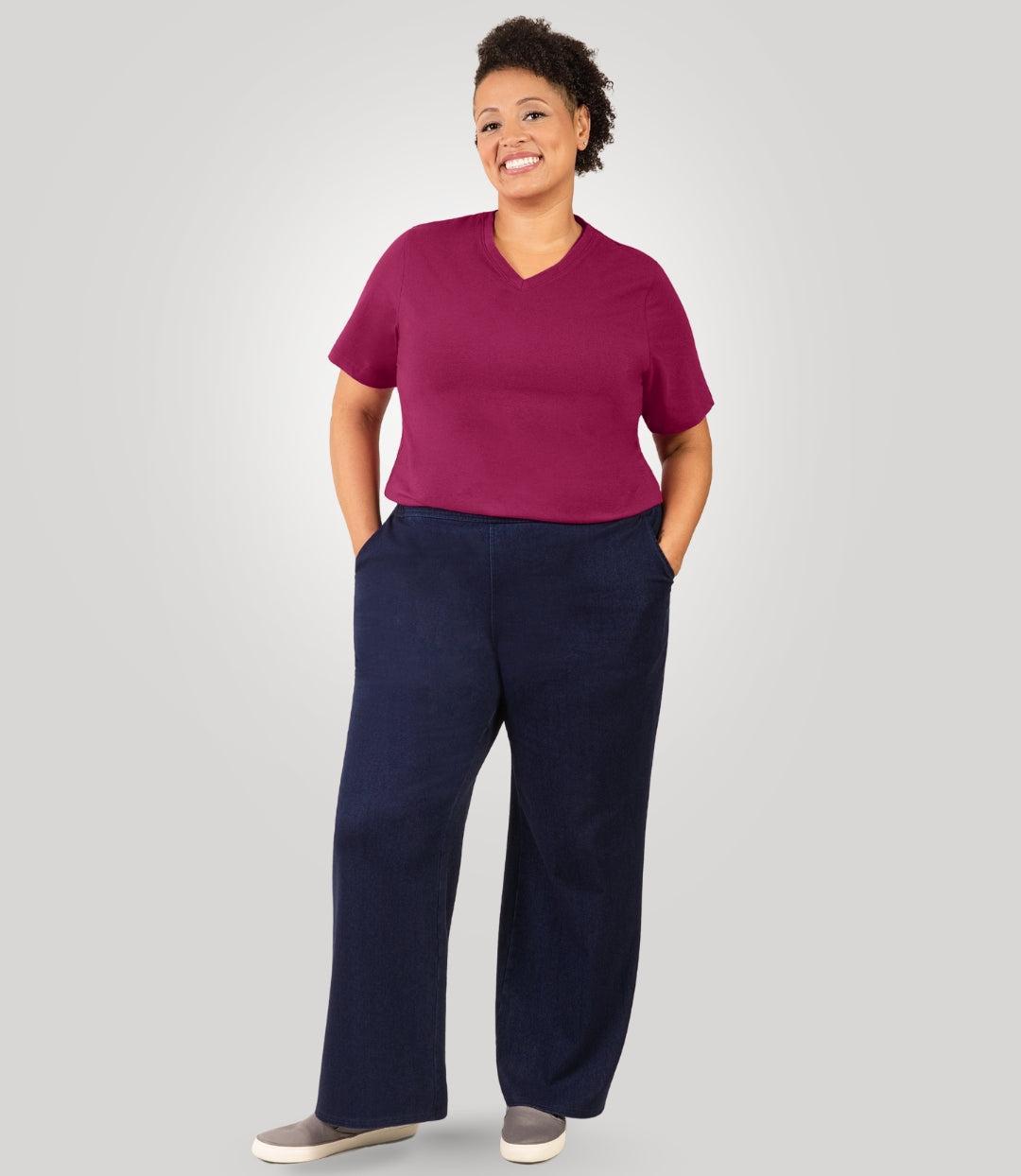 Plus size woman, facing front, wearing JunoActive's Wide Leg Stretch Twill Plus Size Pant. Both hands are in her pant pockets. She's wearing JunoActive's Stretch Naturals V-neck tee in color Merlot. Shirt is tucked into pants to show off fit and banding of twill pant.