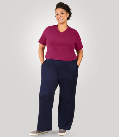 Plus size woman, facing front, wearing JunoActive's Wide Leg Stretch Twill Plus Size Pant. Both hands are in her pant pockets. She's wearing JunoActive's Stretch Naturals V-neck tee in color Merlot. Shirt is tucked into pants to show off fit and banding of twill pant.